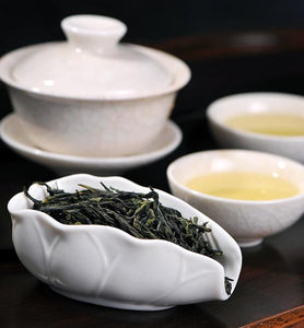green tea leaves beside two cups of brewed green tea