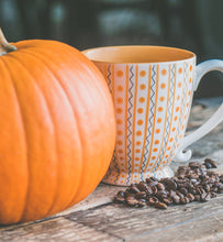 coffee in a blue and orange cup beside a pumpkin