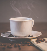 steaming coffee in a white coffee mug beside coffee beans