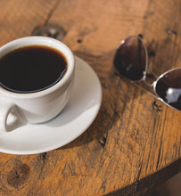 black coffee in white coffee cup beside sunglasses