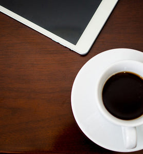 black coffee in white cup beside tablet