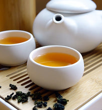 brewed green tea beside white teapot and green tea leaves